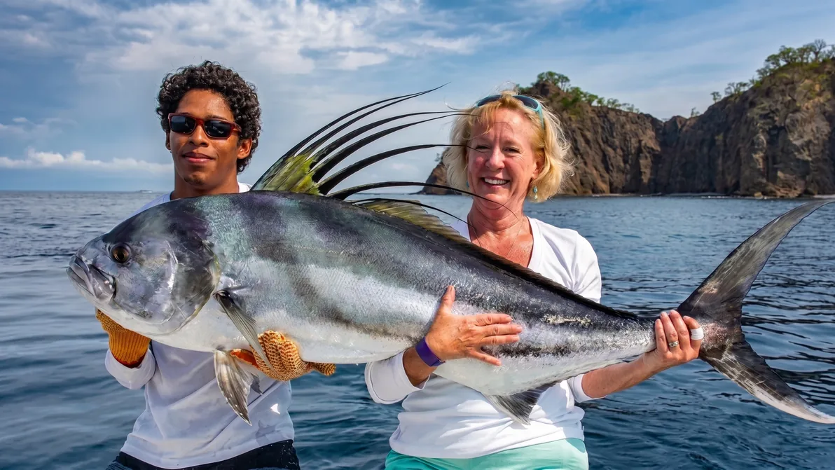 Two anglers hold a roosterfish in front of the cliffs at Peninsula Papagayo, Costa Rica