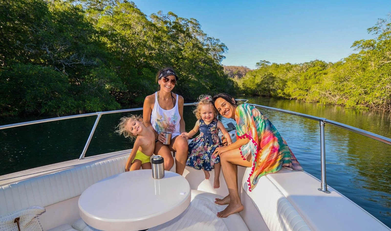 Two women and two small children smiling on the bow of a boat in a calm mangrove estuary