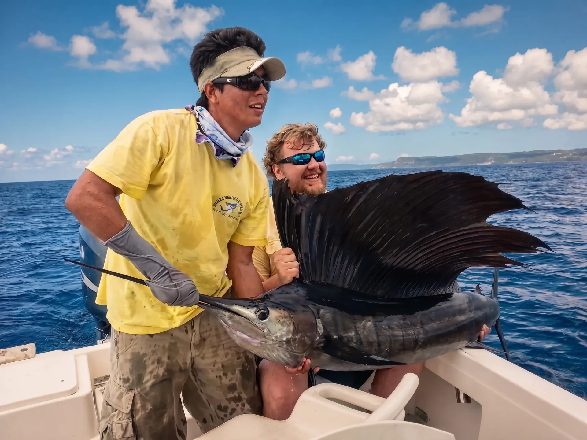 Two crew members holding a sailfish alongside the boat before releasing it, offshore of the Gulf of Papagayo