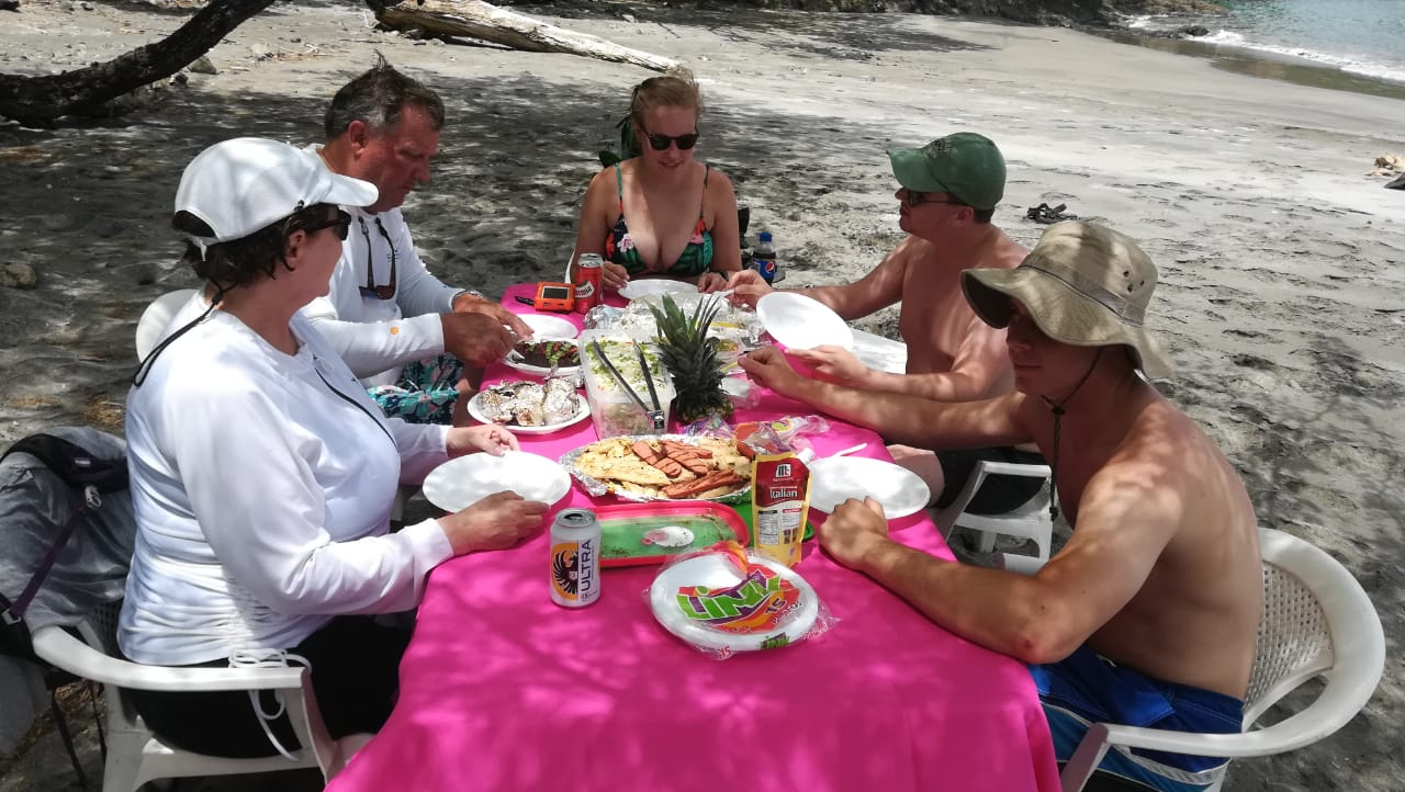 Guests sharing a beach BBQ lunch at a shaded table on a Gulf of Papagayo beach