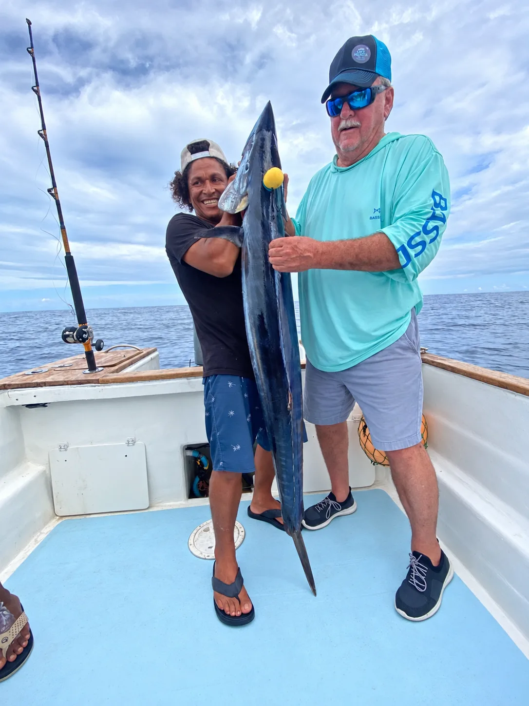 Two anglers hold up a wahoo on the deck of a sport fishing boat, offshore Costa Rica