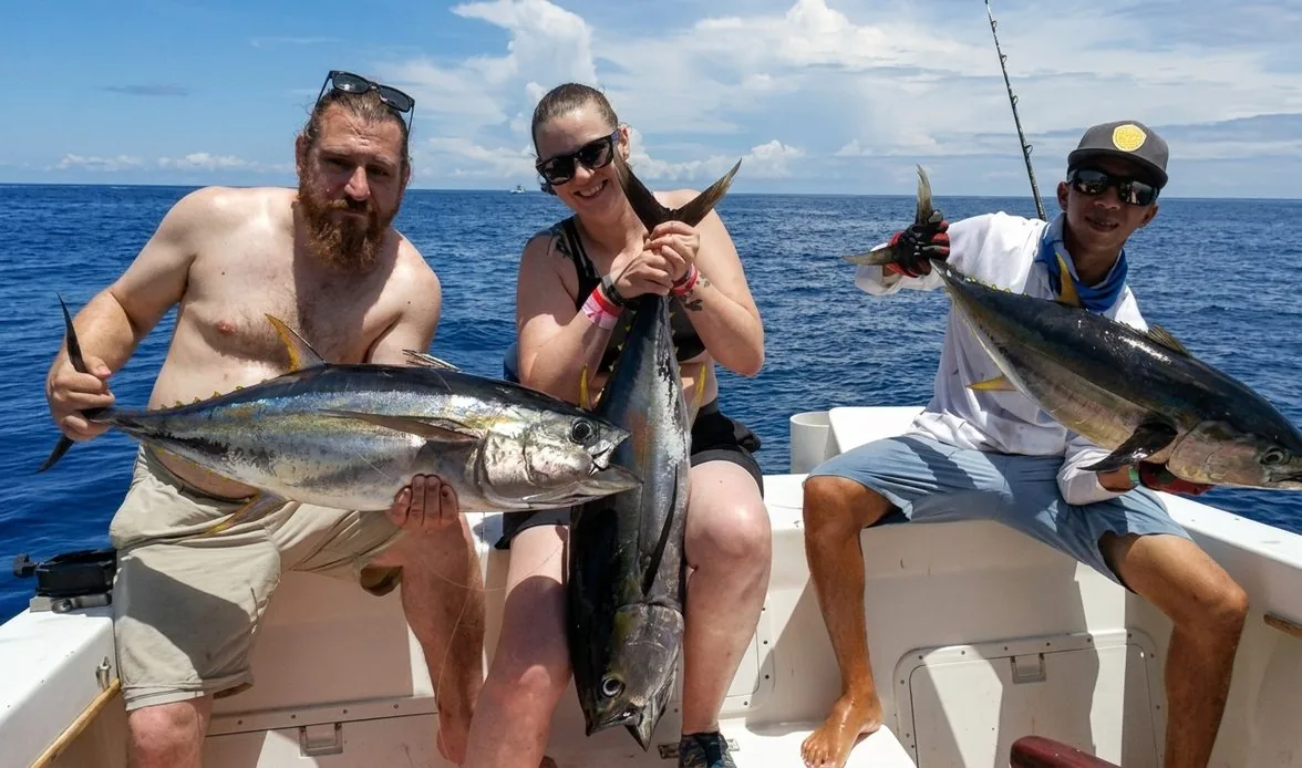 Three anglers with yellowfin tuna on an offshore charter, open Pacific behind them